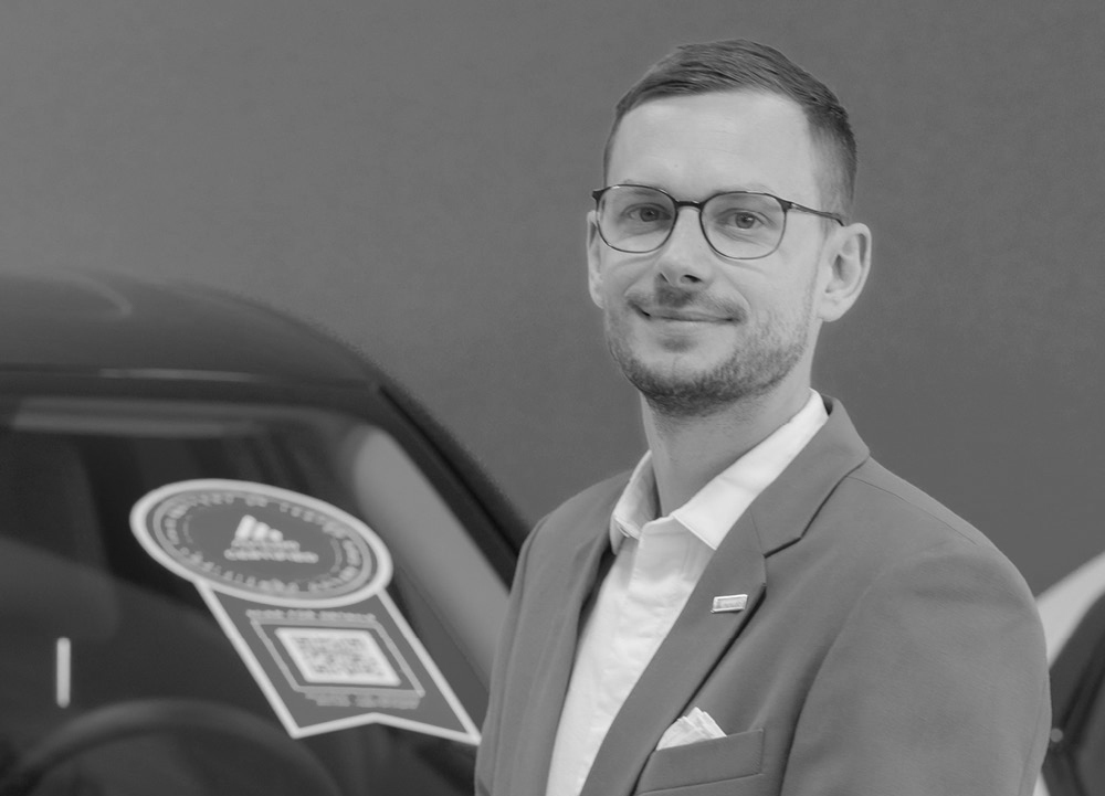 Patrick Schabus, Chief Technical Officer at AVILOO Battery Diagnostics standing by a car in a black and white image