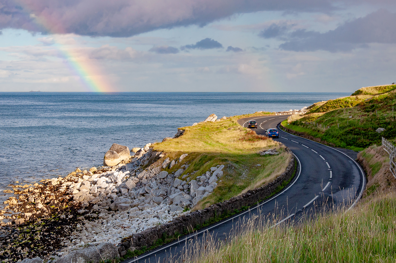 Coastal road in Northern Ireland with sea and a rainbow in the background