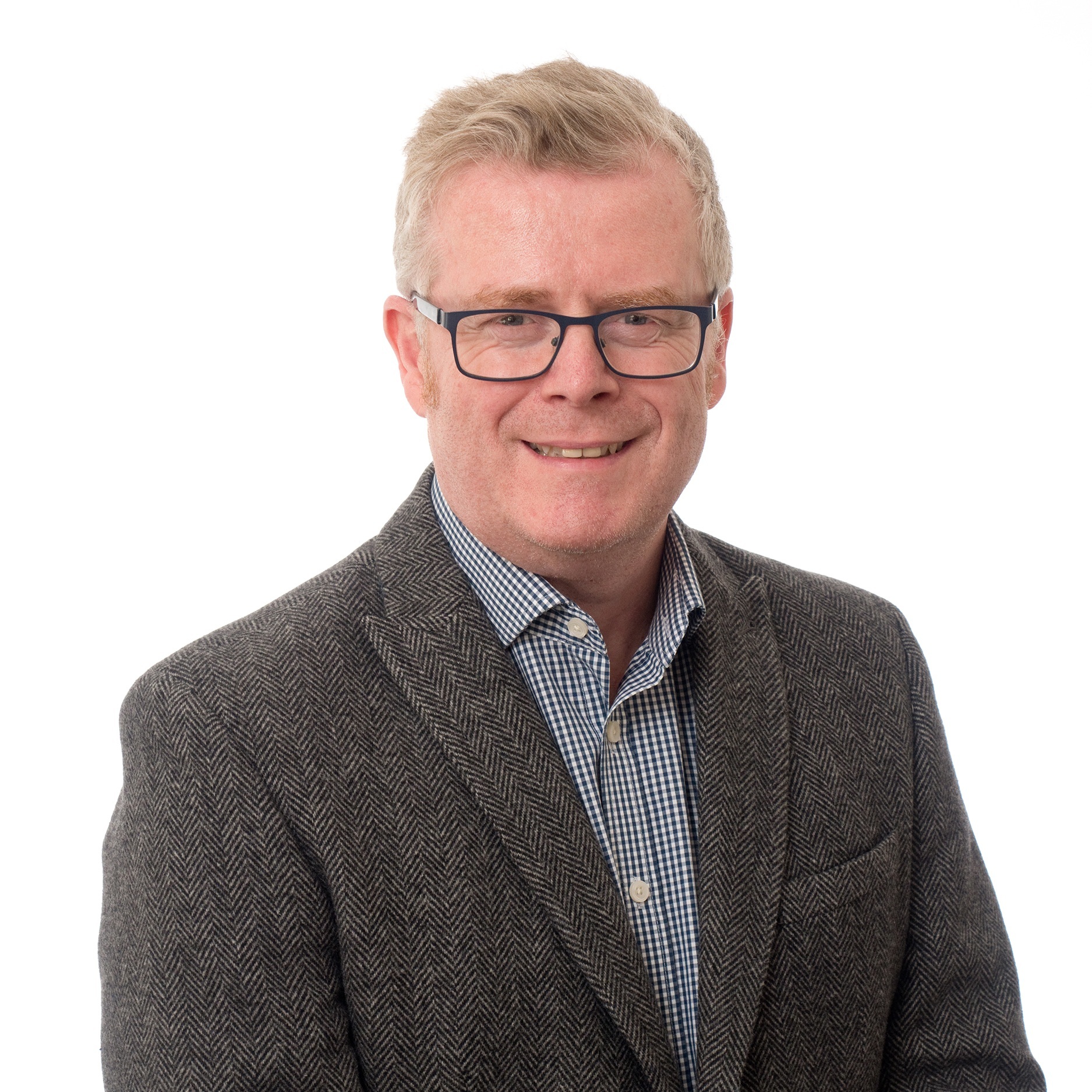 Headshot of Simon Tebbutt on a white background. Simon is wearing glasses, a smart blue-checked shirt and dark grey blazer