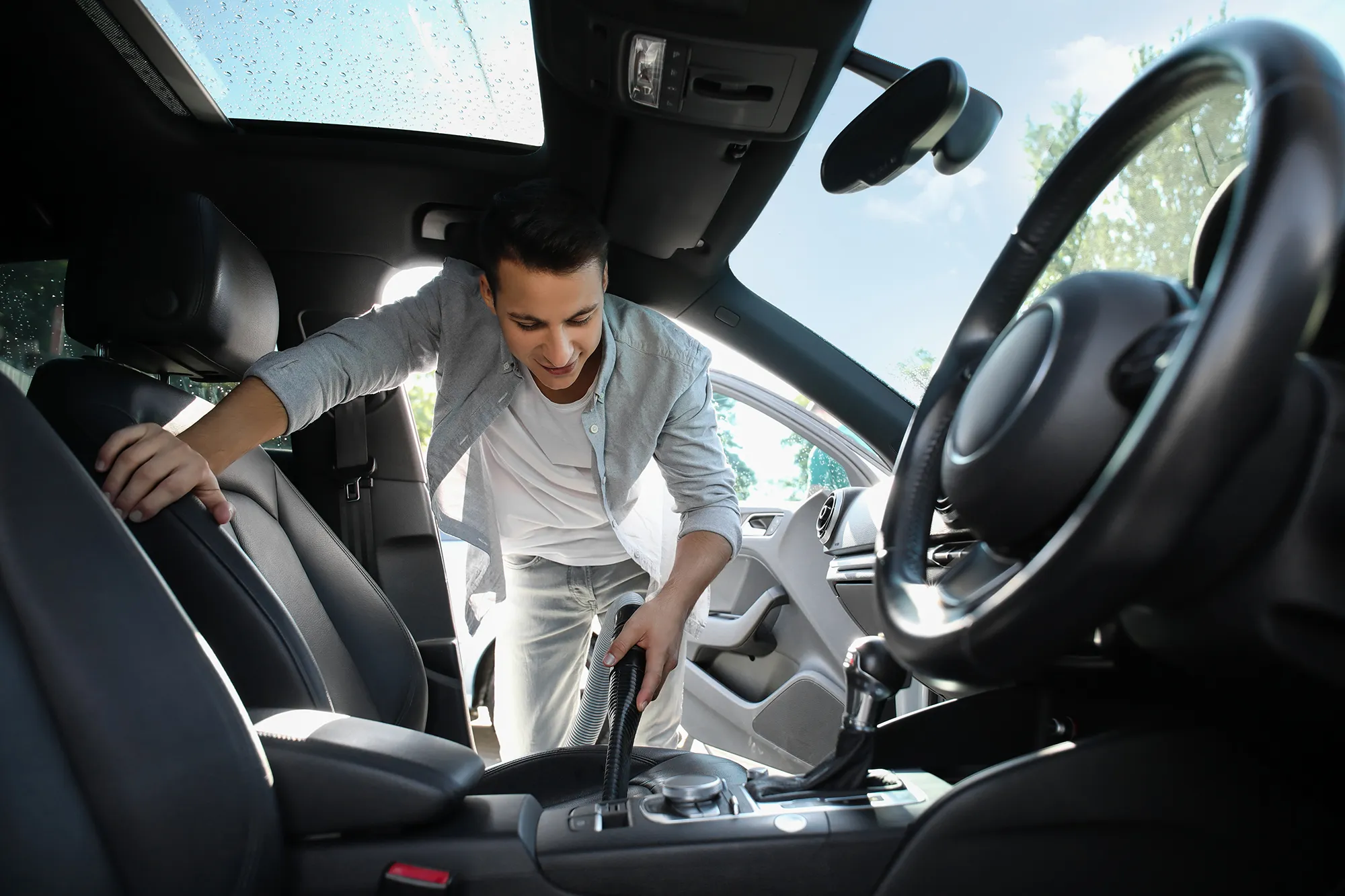Man using a vacuum cleaning on the inside of his car, showing looking after upholstery