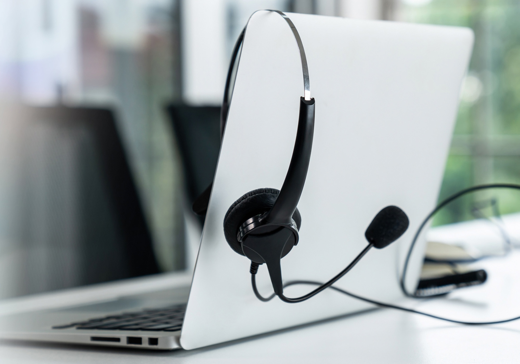 Laptop computer on desk with chair and window in the background, headset hanging over top of laptop