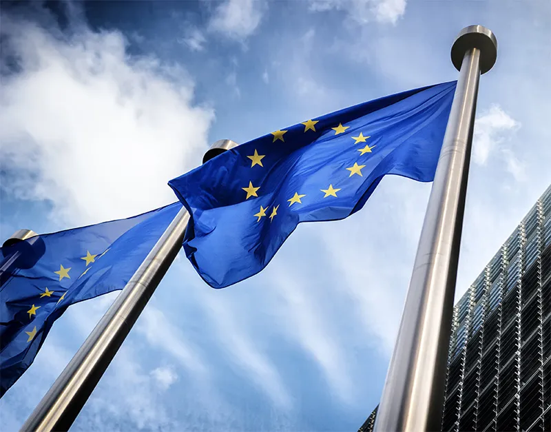 Two flag poles flying flags of the European Union that are blue with yellow stars