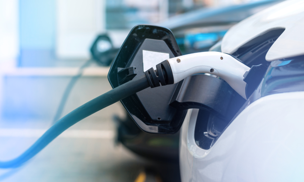 White electric car in foreground connected to charger, blue electric car in background, also connected to charger