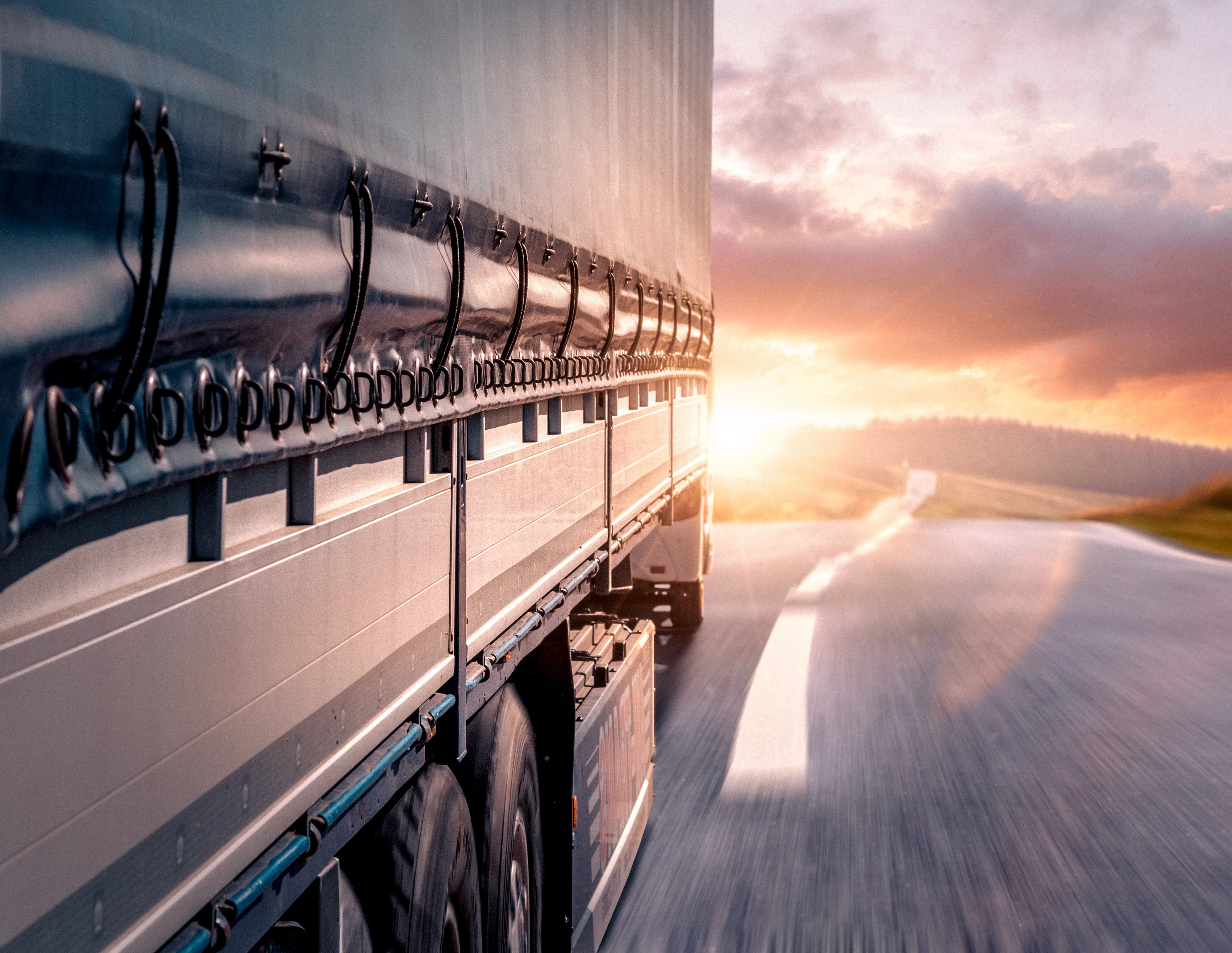 A side view of a Heavy Goods Vehicle HGV on a road driving along, there is a sunset in the background