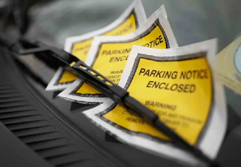 Car windscreen with bright yellow Parking Notice Enclosed envelopes under the windscreen wiper