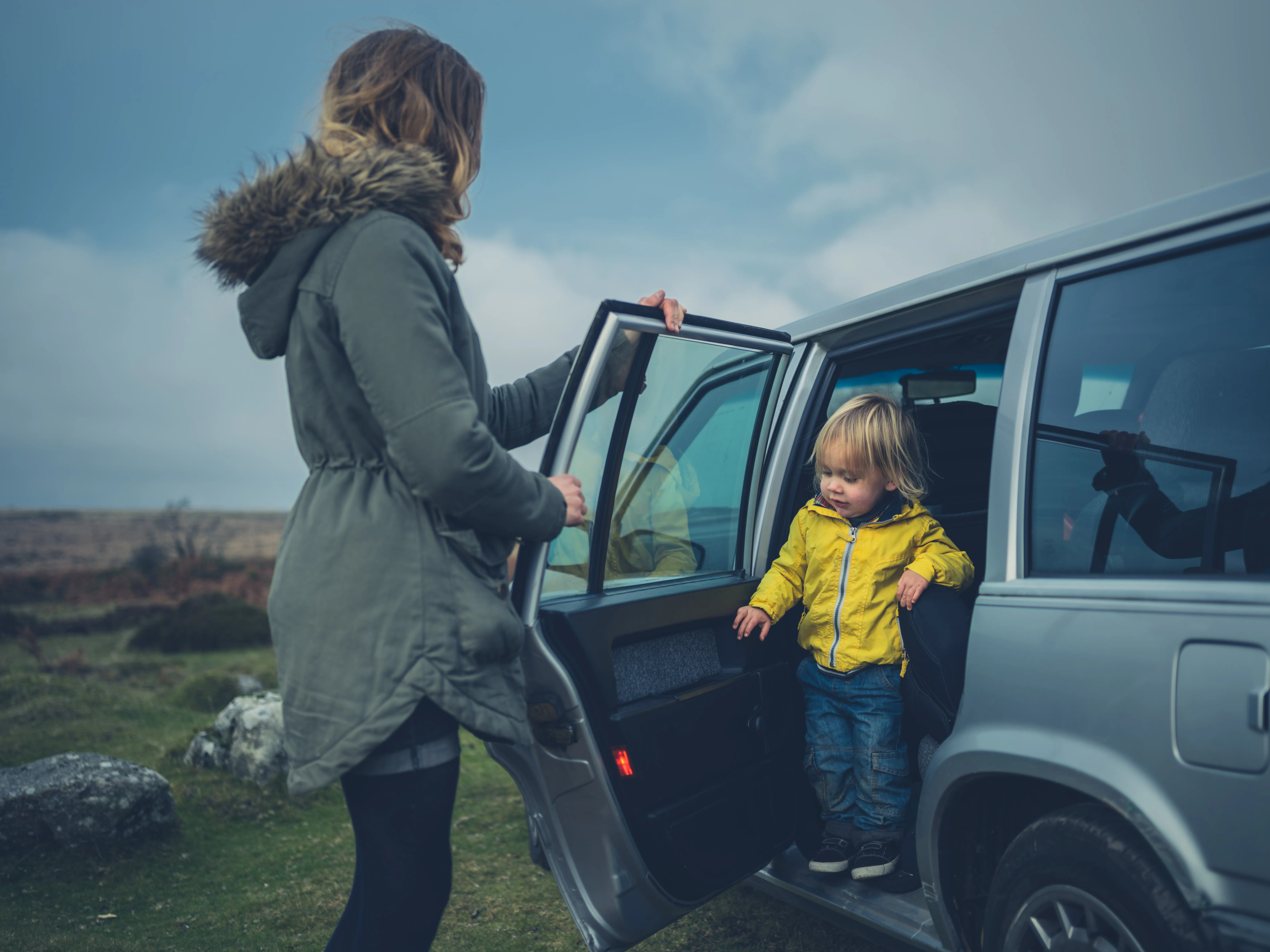 Mother helping toddler get out of car on the moor