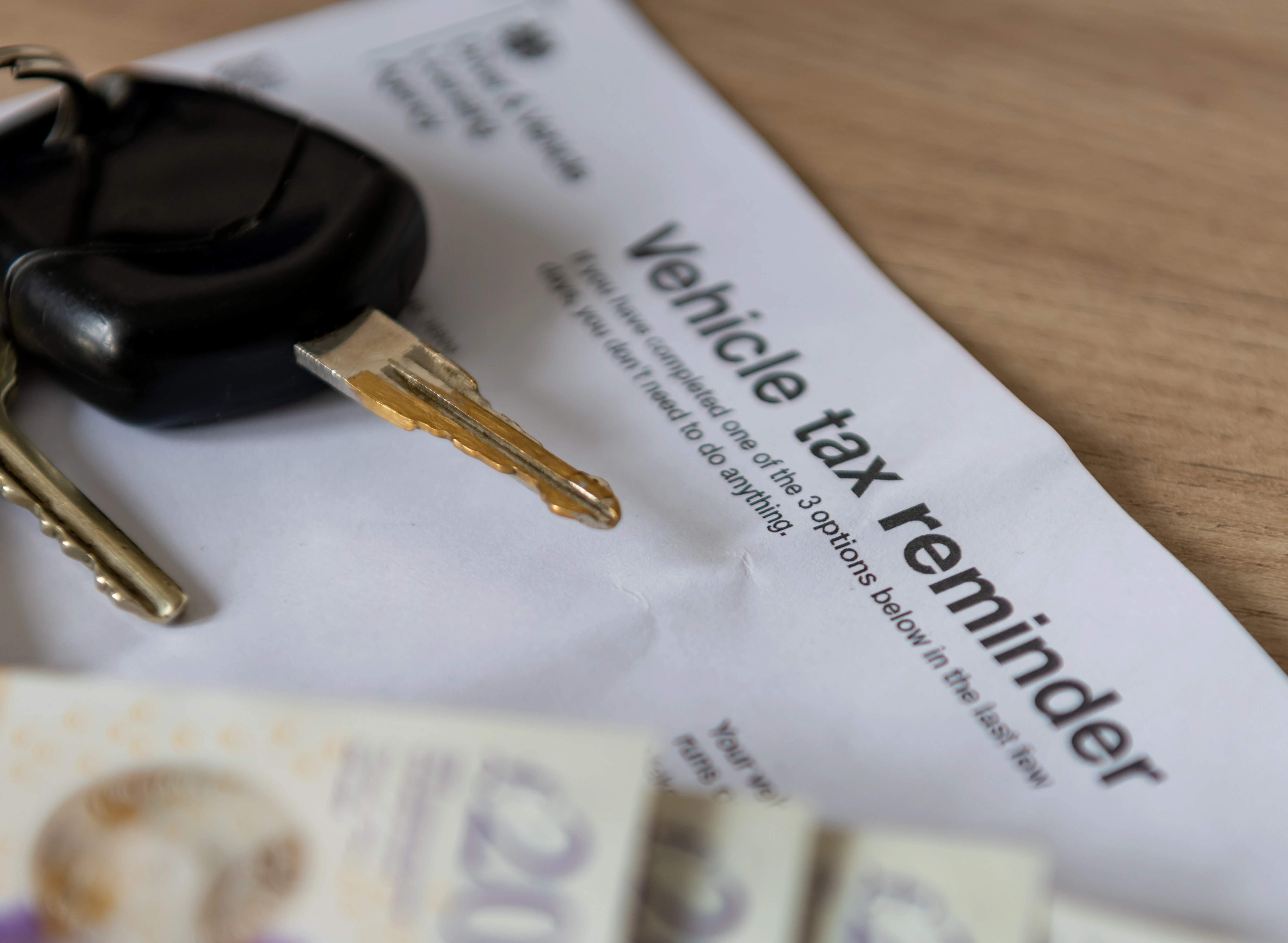 A vehicle tax reminder document of a desk with car keys and money.