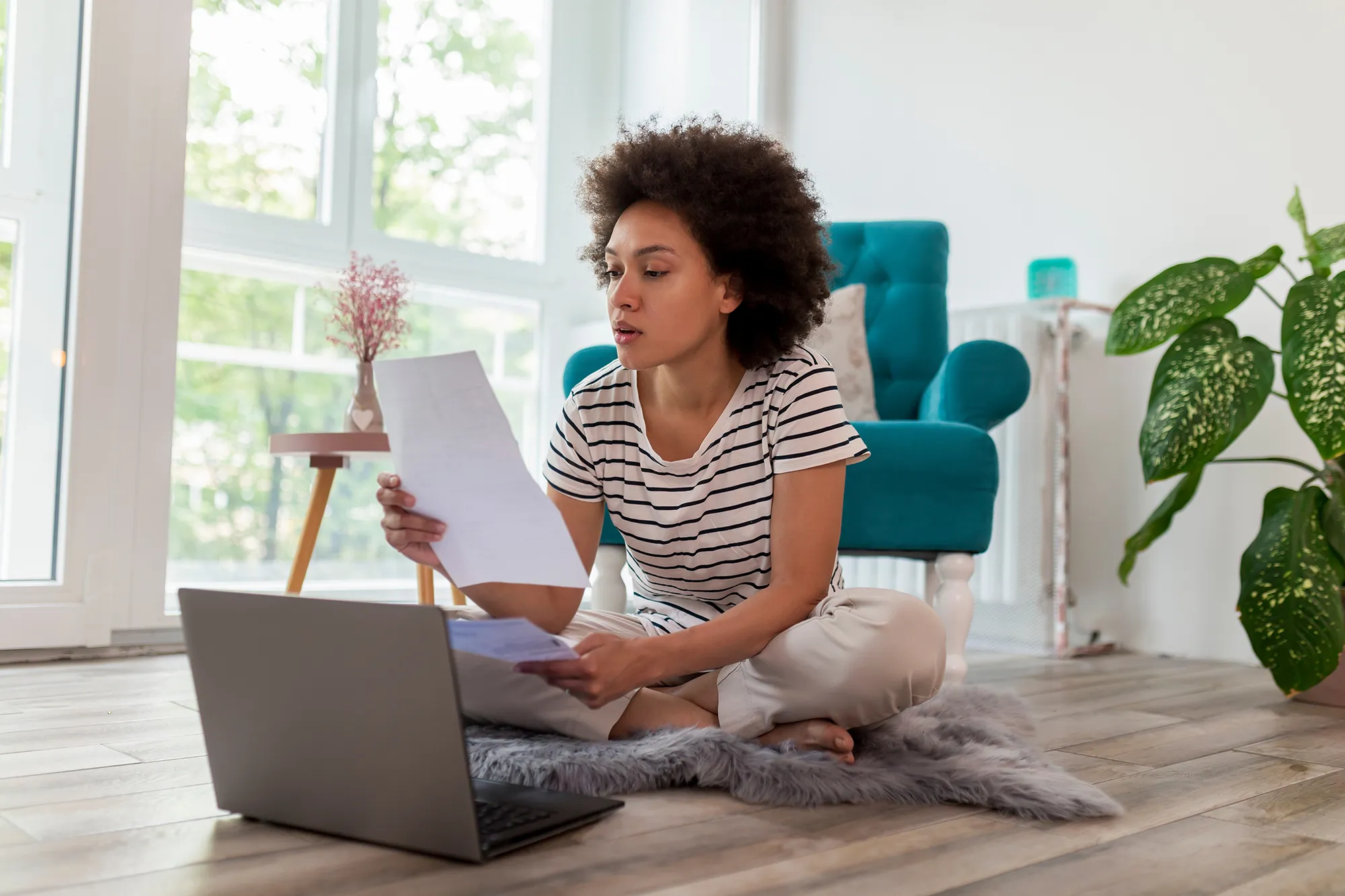 Woman sitting on floor with laptop and papers with a concerned look on her face