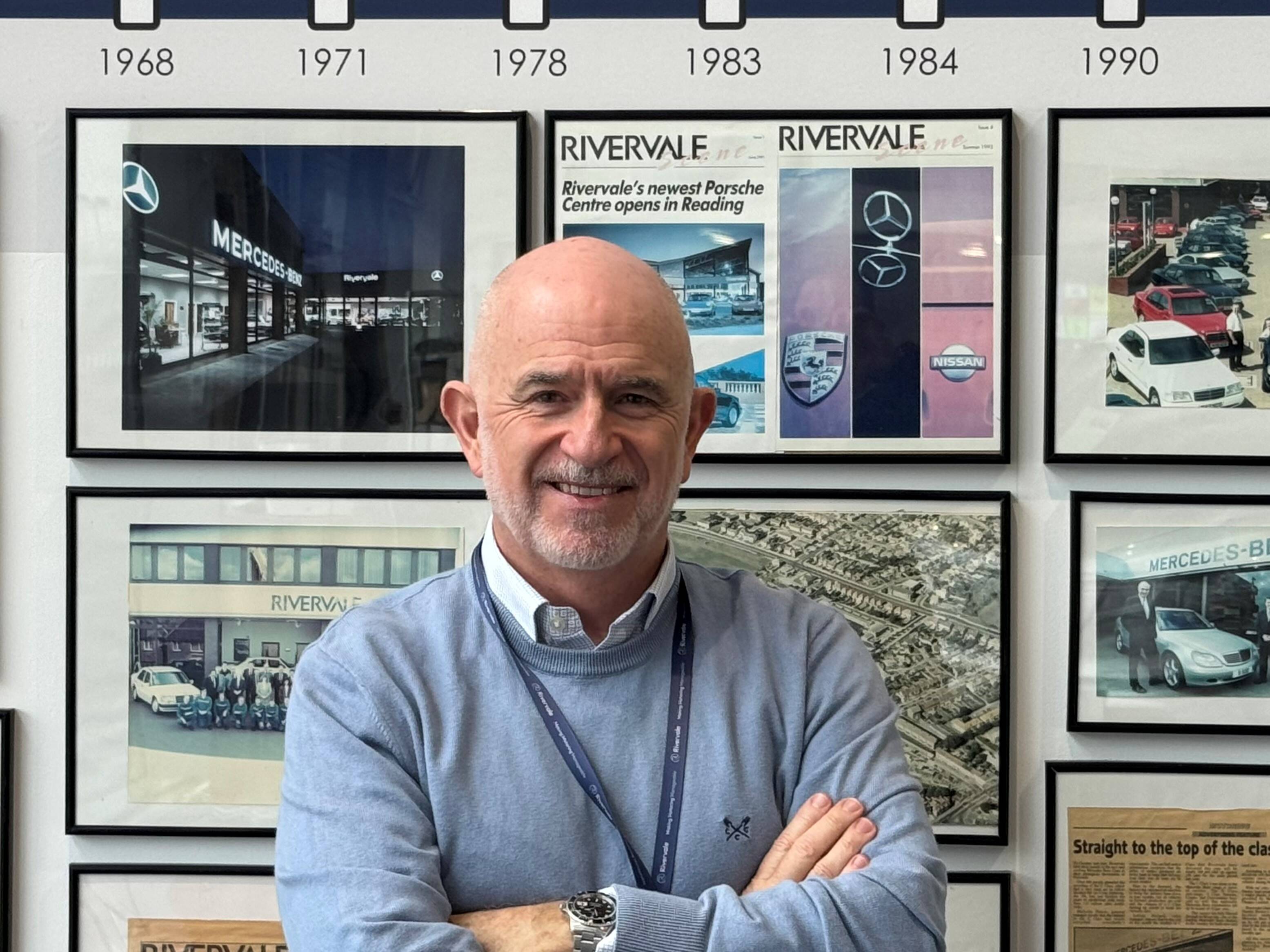 Vince Pemberton stands in front of a wall showing the history of Rivervale. He stands smiling with arms folded
